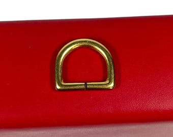 May include: A gold-colored metal D-ring on a red surface.