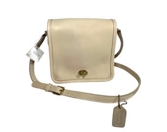 May include: A cream-colored leather crossbody bag with a gold-toned clasp and a Coach brand tag.