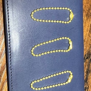 May include: Three gold-colored ball chain keychains on a blue background. Each keychain is about 2 inches long.
