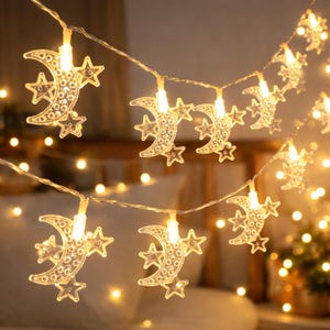 Pode incluir: Fio de luzes decorativas com luas e estrelas de plástico transparente. As luzes são presas em um fio fino e transparente e emitem um brilho amarelo quente. Ideal para ocasiões festivas.