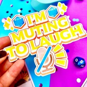 Pu&ograve; includere: Un adesivo giallo con il testo "I'm muting to laugh" e un'icona di microfono blu con una linea rossa che lo attraversa. L'adesivo &egrave; su uno sfondo rosa e blu.