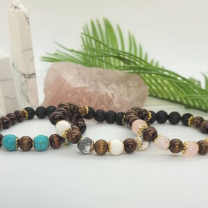 Op de afbeelding: Drie armbanden met verschillende steen- en kralencombinaties. Eén armband heeft turquoise en bruine kralen, een andere heeft witte en grijze kralen, en de derde heeft roze en bruine kralen. Allemaal met goudkleurige accenten.