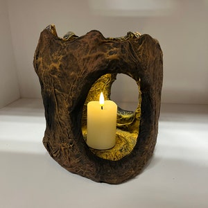 May include: A brown and yellow candle holder made of paper mache with a single white candle inside.