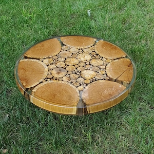 May include: A round wooden coffee table with a unique design featuring a mosaic of wood slices embedded in clear resin. The table has a natural wood finish and a circular shape.