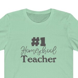 K&ouml;nnte beinhalten: Ein hellgr&uuml;nes T-Shirt mit dem Text "#1 Homeschool Teacher" in Schwarz.