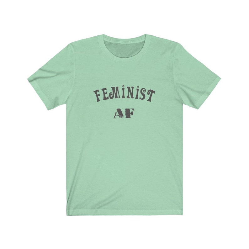 Op de afbeelding: Een lichtgroen T-shirt met de tekst "FEMINIST AF" in zwart.