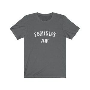 Op de afbeelding: Een donkergrijs T-shirt met de tekst "FEMINIST AF" in wit.
