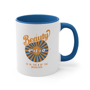 May include: White ceramic mug with a blue rim and handle. The mug features a graphic of a sunburst with the mathematical equation "e^(i*pi) + 1 = 0" in the center. The text "Beauty is in the i of the beholder" is printed below the graphic.