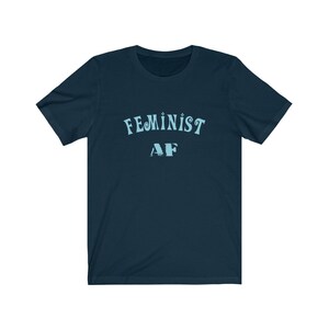 Op de afbeelding: Een marineblauw t-shirt met de tekst "FEMINIST AF" in lichtblauw.