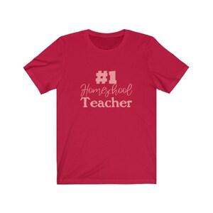 K&ouml;nnte beinhalten: Rotes T-Shirt mit kurzen &Auml;rmeln und dem Text "#1 Homeschool Teacher" in Rosa.