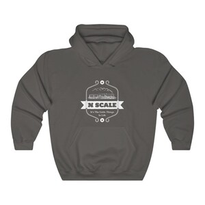 Puede incluir: Una sudadera con capucha gris oscuro con un dise&ntilde;o gr&aacute;fico blanco de un tren y el texto "N SCALE It's The Little Things In Life".