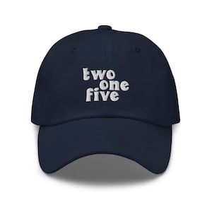 May include: A navy blue baseball cap with the embroidered text "two one five" in white. The cap has a curved brim and a rounded crown, suitable for casual wear.