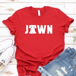 Peut inclure: T-shirt rouge avec un graphique blanc de la Liberty Bell et le mot "JTOWN".