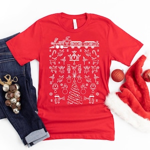 May include: Red t-shirt with a white Christmas-themed design. The design features a train, a Christmas tree, reindeer, snowmen, and other holiday symbols.