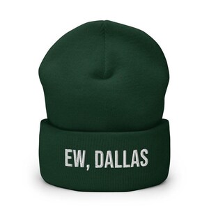 May include: A dark green beanie with a white embroidered design that says "EW, DALLAS".