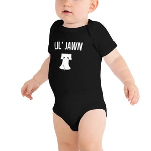 May include: Black baby growsuit with white text that reads "Lil' Jawn" and a white silhouette of the Liberty Bell.