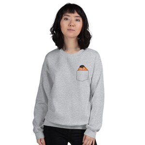 May include: A gray sweatshirt with a front pocket featuring a cartoon character wearing a black hat peeking out of the pocket.