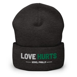 K&ouml;nnte beinhalten: Eine dunkelgraue M&uuml;tze mit einem wei&szlig;en und gr&uuml;nen Stickmuster, auf dem "LOVE HURTS - XOXO, PHILLY -" steht.