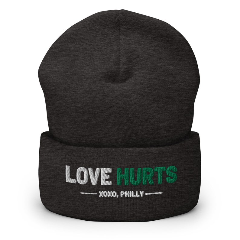K&ouml;nnte beinhalten: Eine dunkelgraue M&uuml;tze mit einem wei&szlig;en und gr&uuml;nen Stickmuster, auf dem "LOVE HURTS - XOXO, PHILLY -" steht.