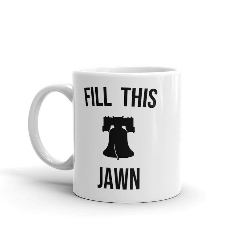 Puede incluir: Taza de cer&aacute;mica blanca con una silueta negra de la Campana de la Libertad y el texto "FILL THIS JAWN".