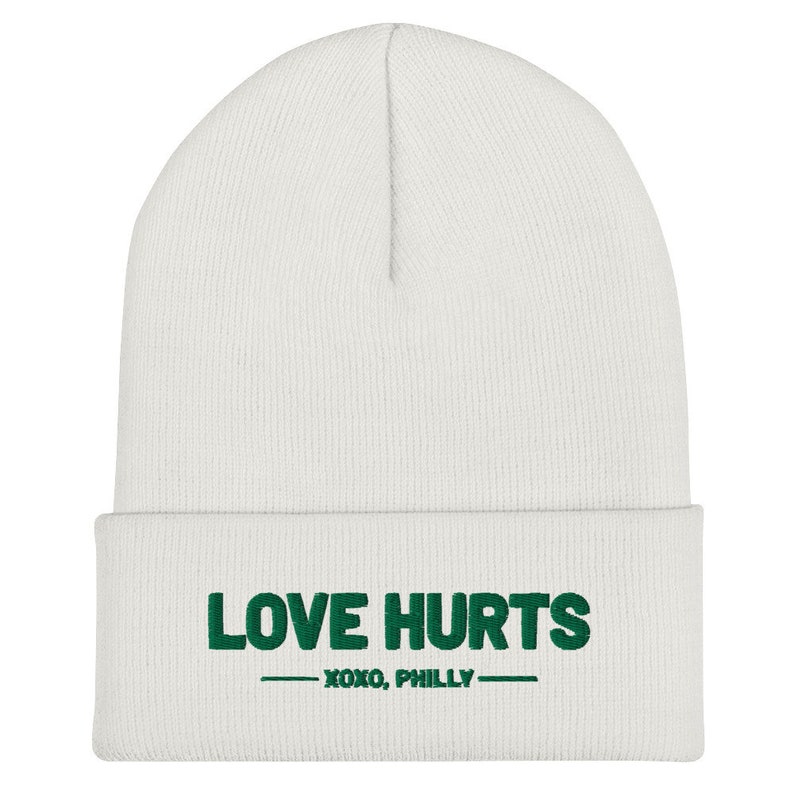 K&ouml;nnte beinhalten: Wei&szlig;e M&uuml;tze mit gr&uuml;nem Sticktext "LOVE HURTS - XOXO, PHILLY -"