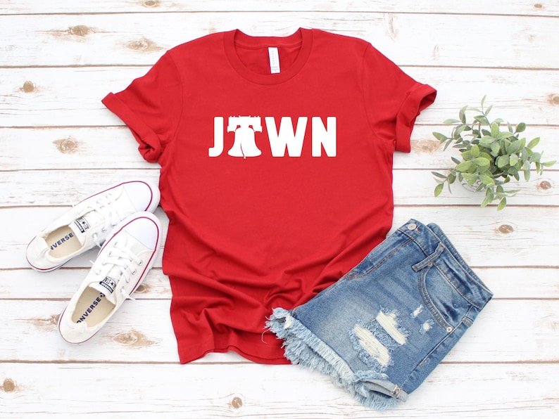 Peut inclure: T-shirt rouge avec un graphique blanc de la Liberty Bell et le mot "JTOWN".