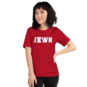 Peut inclure: Un t-shirt rouge &agrave; manches courtes avec un graphique blanc de la Liberty Bell et le mot "Jawn" imprim&eacute; sur le devant.