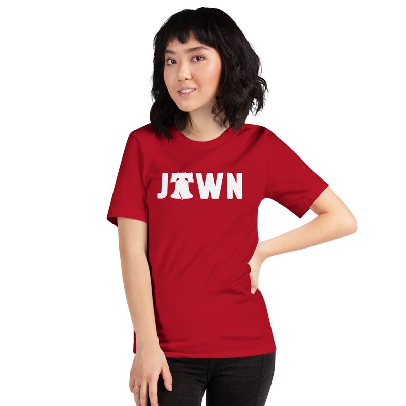 Peut inclure: Un t-shirt rouge &agrave; manches courtes avec un graphique blanc de la Liberty Bell et le mot "Jawn" imprim&eacute; sur le devant.