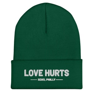 K&ouml;nnte beinhalten: Eine dunkelgr&uuml;ne M&uuml;tze mit dem in Wei&szlig; gestickten Text "LOVE HURTS - XOXO, PHILLY -."