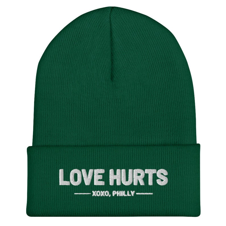 K&ouml;nnte beinhalten: Eine dunkelgr&uuml;ne M&uuml;tze mit dem in Wei&szlig; gestickten Text "LOVE HURTS - XOXO, PHILLY -."