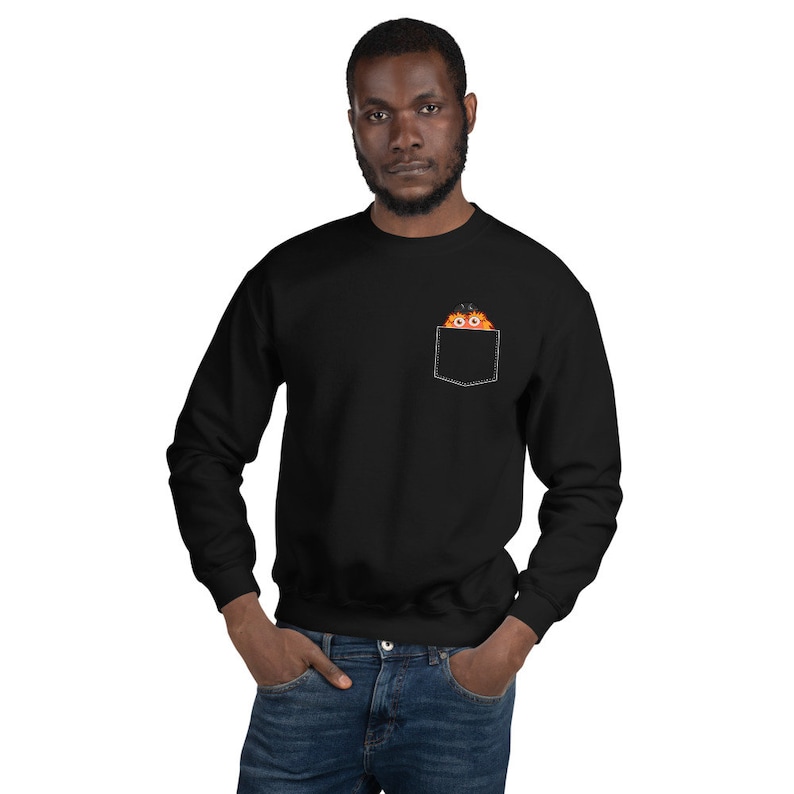 May include: A black sweatshirt with a front pocket featuring a cartoon orange monster peeking out. The monster has a black hat and large eyes.