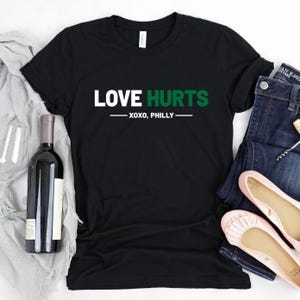 May include: Black t-shirt with white text that reads "LOVE HURTS - XOXO, PHILLY" in green.