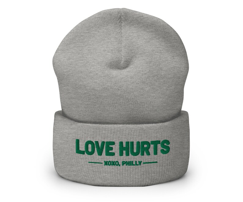 K&ouml;nnte beinhalten: Graue M&uuml;tze mit einem gr&uuml;nen gestickten Design, das "LOVE HURTS - XOXO, PHILLY -" sagt.