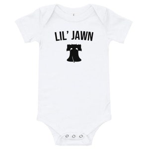 May include: White baby grow with black text that reads "Lil' Jawn" and a black silhouette of the Liberty Bell.