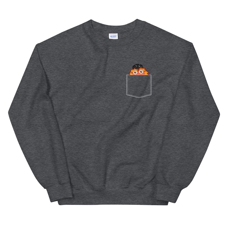 May include: A dark gray sweatshirt with a front pocket featuring a cartoon monster peeking out. The monster is orange and black with large eyes.