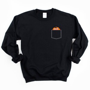 May include: Black sweatshirt with a pocket featuring a cartoon character with orange fur and a black hat peeking out of the pocket.