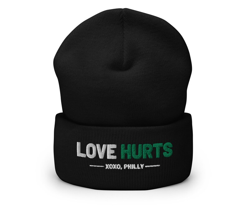 K&ouml;nnte beinhalten: Schwarze M&uuml;tze mit einem wei&szlig;en und gr&uuml;nen Stickmuster, auf dem "LOVE HURTS - XOXO, PHILLY -" steht.