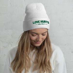 K&ouml;nnte beinhalten: Wei&szlig;e M&uuml;tze mit dem Text "LOVE HURTS - XOXO, PHILLY -" in gr&uuml;ner Stickerei.