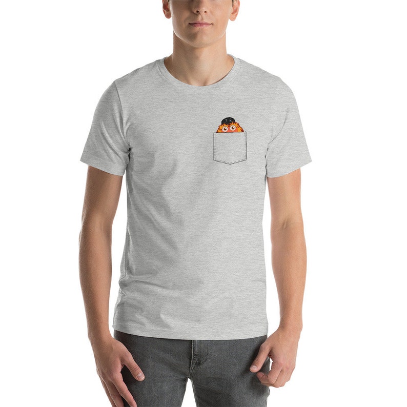 May include: A gray t-shirt with a pocket featuring a cartoon character with orange fur, a black hat, and large eyes.