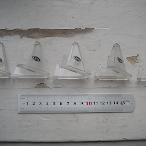 以下が含まれることがあります： 透明なプラスチック製のディスプレイスタンドが5つあり、それぞれに「CASE」と印刷されています。スタンドは白い木製の表面に一列に並べて置かれています。スタンドの下には定規が置かれています。