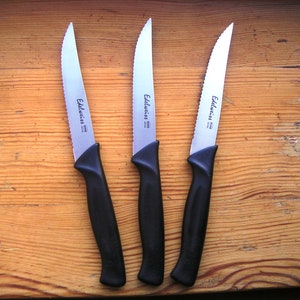 以下が含まれることがあります： 黒い柄の銀色のギザギザのステーキナイフが3本。ナイフには刃の側面に「Edelweiss」と印刷されています。