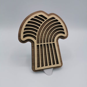 May include: A wooden wall decoration in the shape of a stylised tree with a brown wood finish. The tree has a rounded top and a long, thin trunk with a decorative pattern.