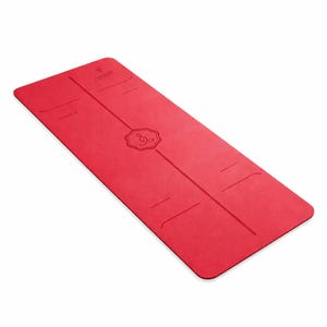 May include: A red yoga mat with a textured surface. The mat has embossed alignment lines and a central design. The brand name and logo are visible at the top. The mat is rectangular and designed for exercise.