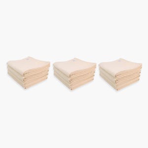 May include: Three stacks of beige cotton fabric cloths, each stack containing ten cloths.