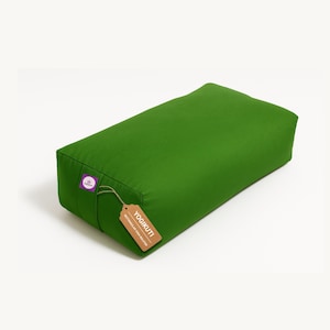 Puede incluir: Un cojín de yoga rectangular verde con una etiqueta que dice "YOGIKUTI RECTANGULAR YOGA BOLSTER". El cojín es de color verde sólido y vibrante y parece estar hecho de una tela duradera. Una pequeña etiqueta morada con una estrella blanca está adjunta.