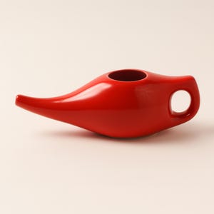 May include: A vibrant red ceramic neti pot with a long spout and a handle with a circular opening. The neti pot is designed for nasal irrigation and has a smooth, glossy finish. The product is a health and wellness item.