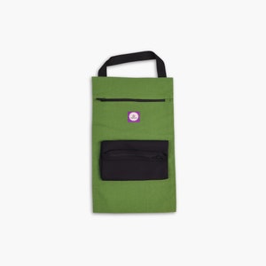 Può includere: Una borsa di tela verde con un manico nero e una tasca con cerniera nera. La borsa ha un piccolo cerchio viola con una stella al centro.