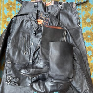 以下が含まれることがあります： 黒い革のジャケット、パンツ、ブーツのセット。 ジャケットには襟、ジッパーポケット、バックルのディテールがあります。 パンツにはサスペンダーとジッパーが付いています。 ブーツはニーハイです。 セットは模様のある表面に表示されます。