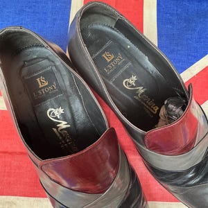 K&ouml;nnte beinhalten: Ein Paar Vintage-Lederschuhe mit einem einzigartigen Farbblock-Design. Die Schuhe weisen eine Kombination aus schwarzen, grauen und weinroten Lederpaneelen auf. Das Innere der Schuhe ist schwarz mit goldfarbenen Buchstaben "L'STONY" und "Morina".