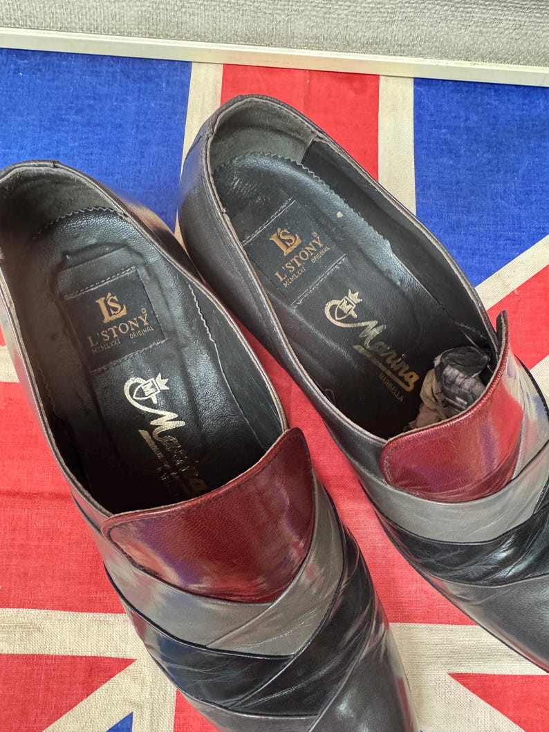 K&ouml;nnte beinhalten: Ein Paar Vintage-Lederschuhe mit einem einzigartigen Farbblock-Design. Die Schuhe weisen eine Kombination aus schwarzen, grauen und weinroten Lederpaneelen auf. Das Innere der Schuhe ist schwarz mit goldfarbenen Buchstaben "L'STONY" und "Morina".